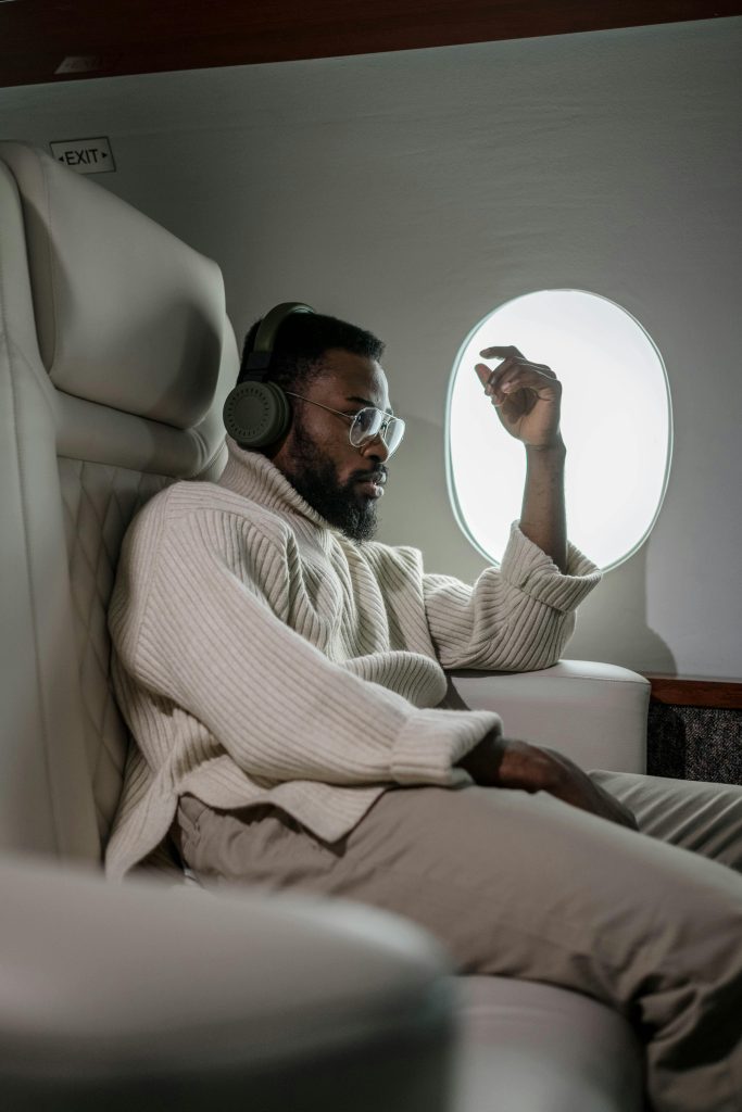 A man enjoying comfort in airplane business class, wearing headphones and lounging by the window.